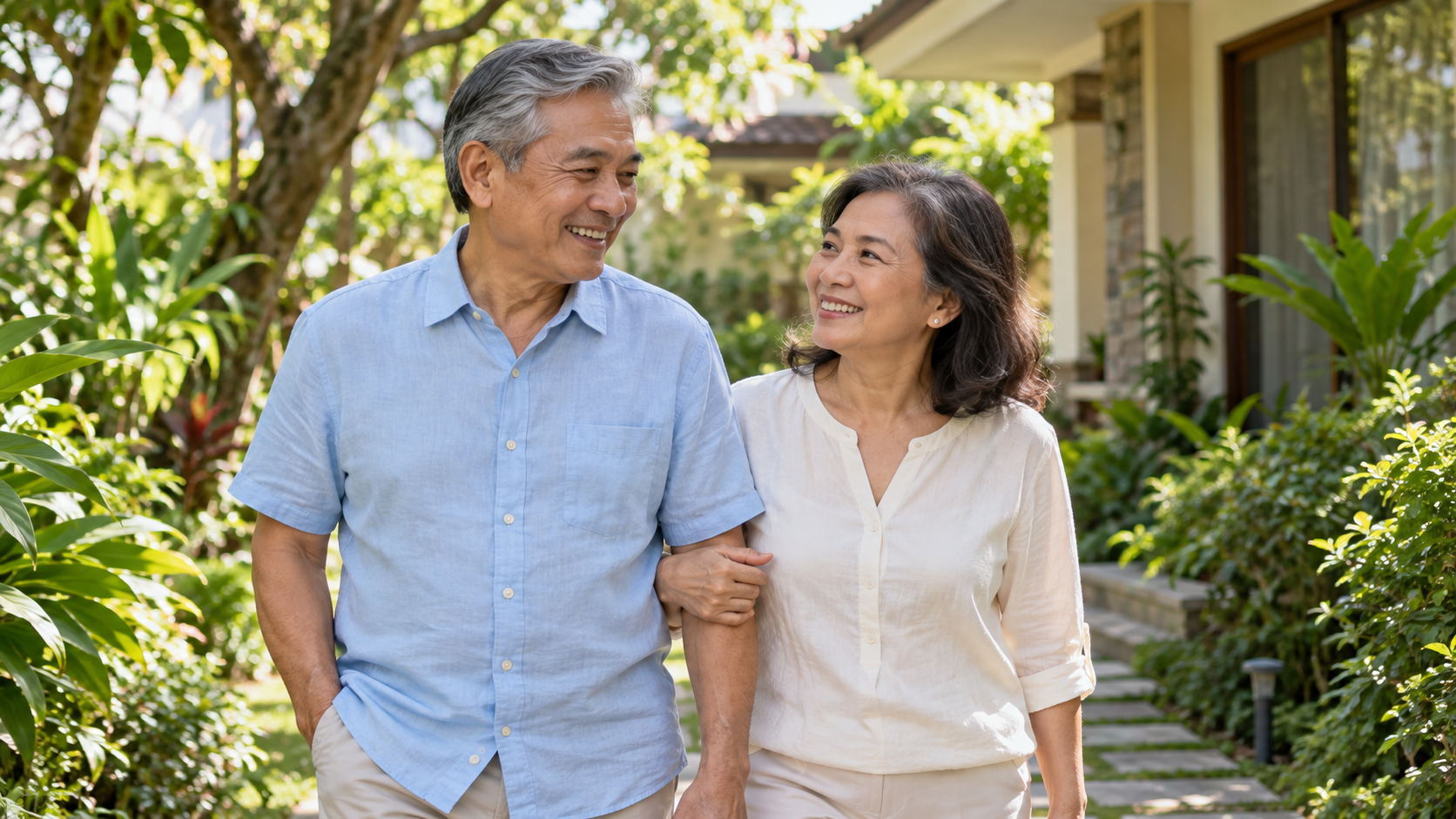 Older Filipino couple walking together in a leafy garden.